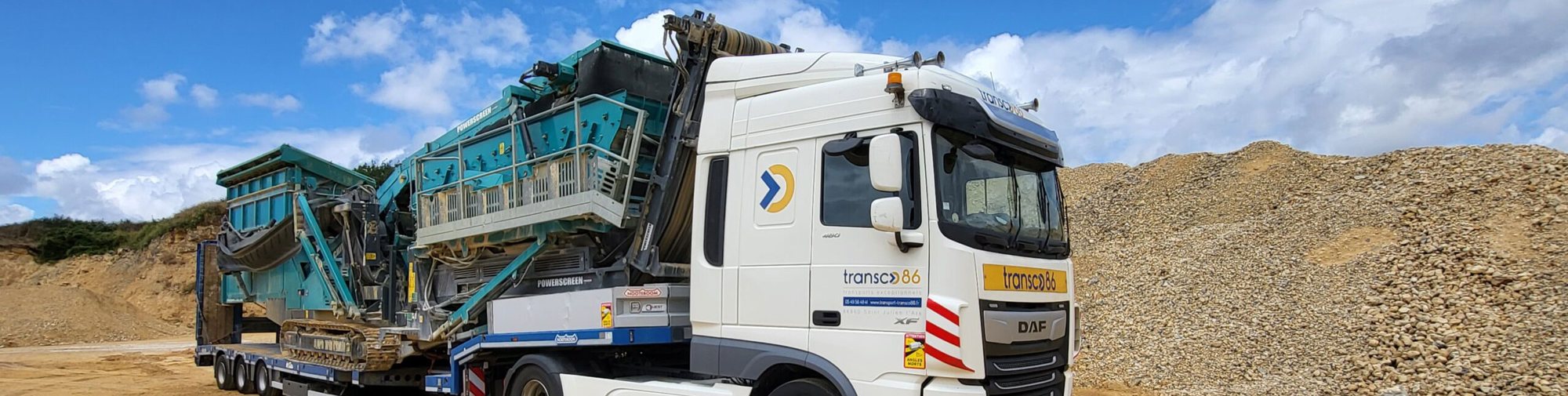 Camion DAF blanc Transco 86 transportant un concasseur sur une carrière