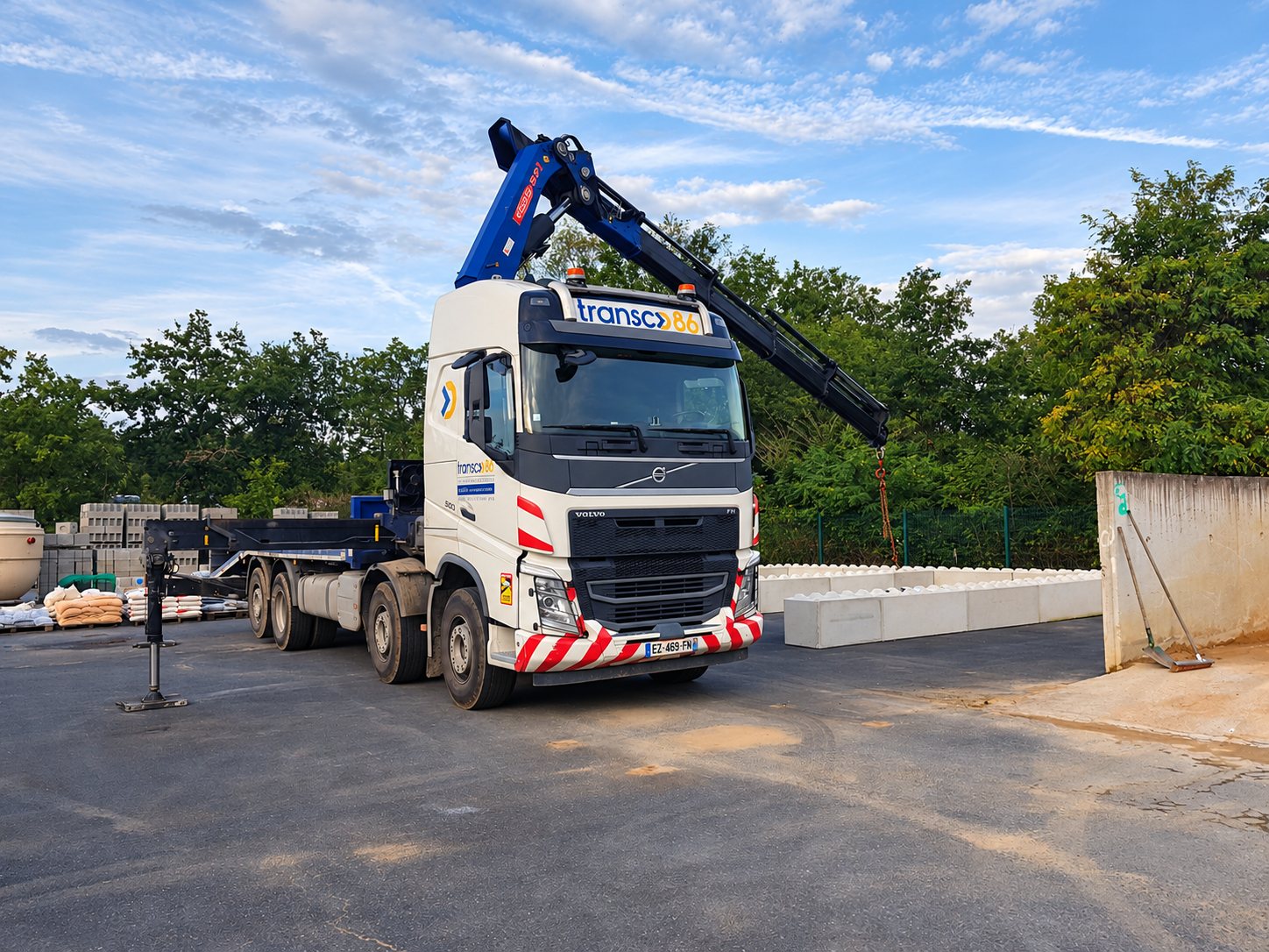 Camion Volvo blanc Transco 86 équipé d’une grue articulée sur un dépôt de matériaux